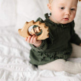 infant holding organic wooden baby rattle shaped like a hedgehog.