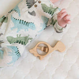 wooden dinosaur baby rattle laying next to infant in a dinosaur outfit.